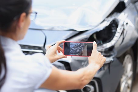 Woman takes a photo of vehicle damage using her phone